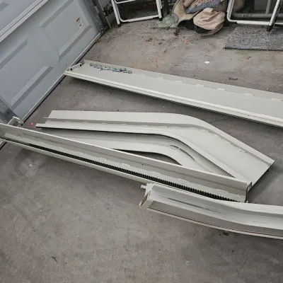 Sale Photo Thumbnail #56: Disassembled modern beige stairlift tracks with integrated gear teeth and assembly hardware lying on a concrete garage floor.