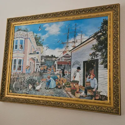Sale Photo Thumbnail #11: Large framed art print depicting a busy coastal village scene with a tall ship, houses, and townspeople, housed in an ornate gold-finished frame.