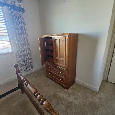Sale Photo Thumbnail #79: Traditional wooden armoire chest with raised panel cabinet doors above two lower drawers, showing a spool-turned bed frame in the foreground.