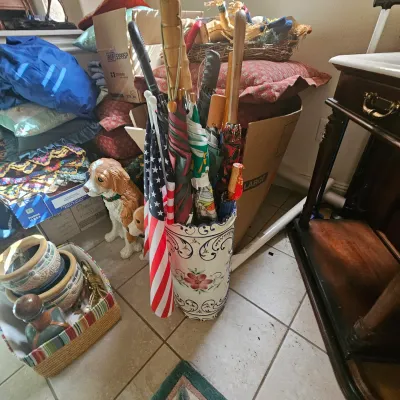 Sale Photo Thumbnail #8: A collection of umbrellas, walking sticks, and a small American flag stored inside a hand-painted ceramic umbrella stand, surrounded by various household goods and a dog figurine.