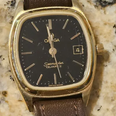 Sale Photo Thumbnail #95: Vintage Omega Seamaster Quartz wristwatch with gold-tone TV dial case, black face, date window, and brown leather strap.