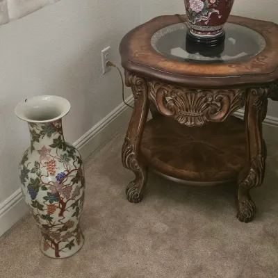 Sale Photo Thumbnail #12: Large Asian-style porcelain floor vase decorated with a grapevine motif, alongside an ornate carved wooden end table with a glass top insertion.