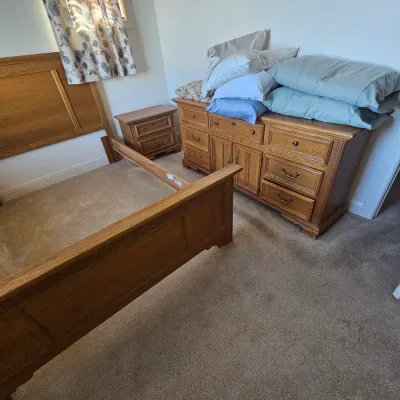 Sale Photo Thumbnail #75: Traditional oak bedroom furniture set including a wooden bed frame, matching nightstand, and large triple dresser with metal hardware.