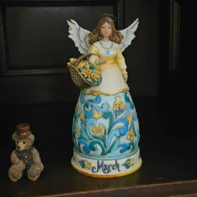 Sale Photo Thumbnail #31: Jim Shore Heartwood Creek "March" angel figurine with a flower basket, displayed alongside a small resin teddy bear figurine.