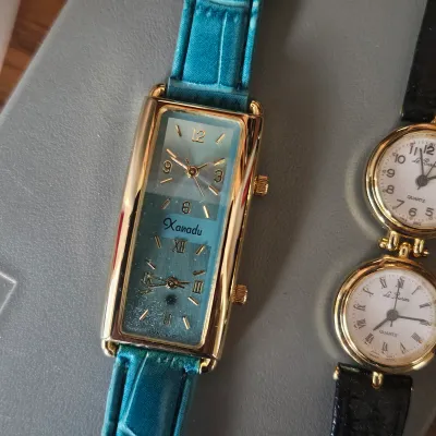 Sale Photo Thumbnail #51: Vintage Xanadu dual-time-zone tank wrist watch featuring a gold-tone case, teal dial, and matching embossed leather strap.