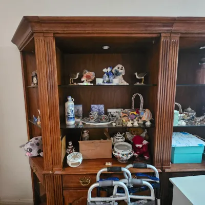 Sale Photo Thumbnail #23: Large wooden display hutch with glass shelves, filled with assorted porcelain figurines, tea sets, plush animals, and decorative collectibles.