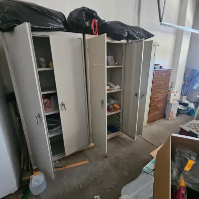 Sale Photo Thumbnail #57: Pair of tall gray metal storage cabinets with double doors and interior shelving, set up in a garage or storage area.