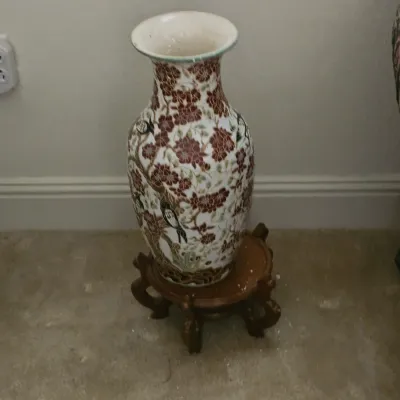 Sale Photo Thumbnail #18: Large Asian-style ceramic floor vase featuring a floral and bird motif in shades of red, green, and brown, displayed on a carved wooden base.