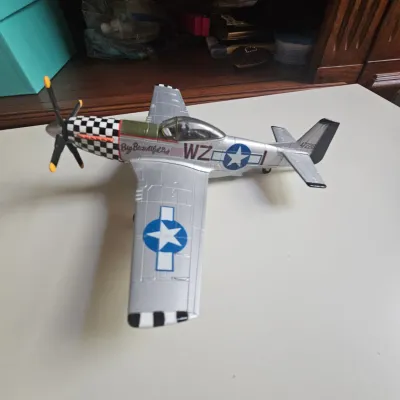 Sale Photo Thumbnail #24: Detailed model airplane replica of a WWII P-51D Mustang labeled "Big Beautiful Doll," featuring silver paint and checkered nose art.