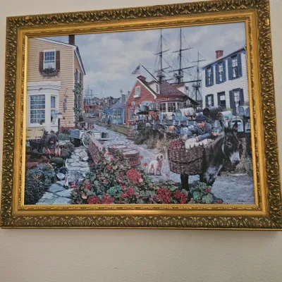 Sale Photo Thumbnail #10: Framed art print depicting a detailed historic harbor village scene, housed in an ornate gold-finished frame.