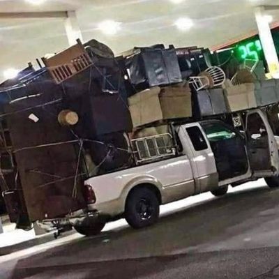 Sale Photo Thumbnail #256: White pickup truck excessively overloaded with an assortment of household furniture, including sofas, chairs, and wooden cabinets.
