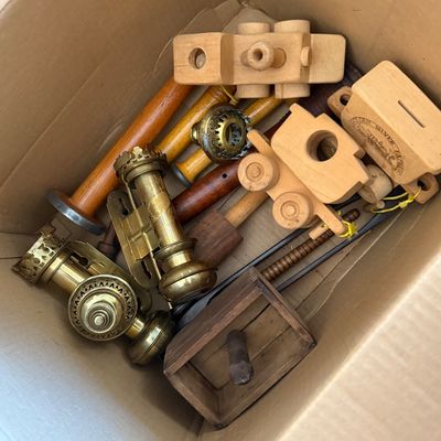 Sale Photo Thumbnail #90: Cardboard box containing a mix of vintage wooden items including toy train cars and bobbins, alongside brass oil lamp burner parts.