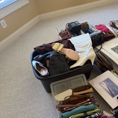 Sale Photo Thumbnail #23: Collection of women's shoes, boots, and handbags displayed in storage bins on a carpeted floor, including a pair of white high-heeled boots and a metallic chain sandal.