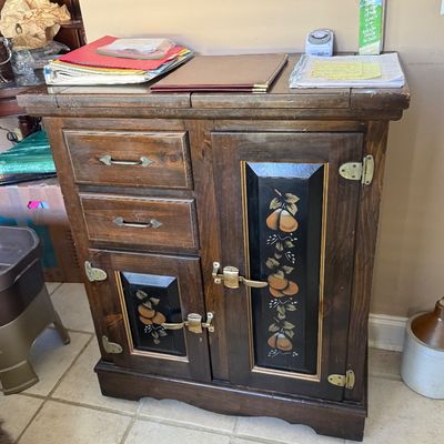 Sale Photo Thumbnail #82: Vintage dark-stained wooden icebox-style cabinet featuring hand-painted fruit accents on black inset panels and decorative brass hardware.