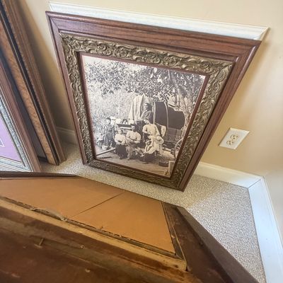 Sale Photo Thumbnail #171: Framed sepia-tone photograph depicting an early pioneer family gathered near a covered wagon, housed in an ornate carved wood and gilt frame.