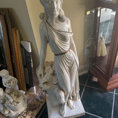 Sale Photo Thumbnail #117: Classical neoclassical-style floor statue of a draped female figure with gold trim, standing beside smaller decorative cherub statues.