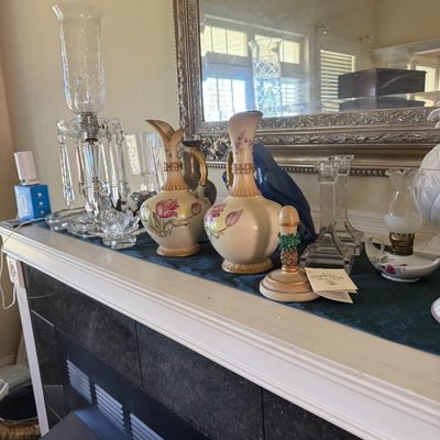 Sale Photo Thumbnail #33: Collection of tabletop decor displayed on a mantel, including a pair of floral ceramic ewers, a cut crystal hurricane lamp, clear glass candlesticks, and a blue porcelain bird figure.