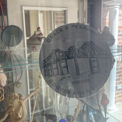 Sale Photo Thumbnail #126: Commemorative Grace & Pearman Cooper River Bridges silver plate or coaster (1929–2005) displayed on an acrylic stand inside a glass cabinet.