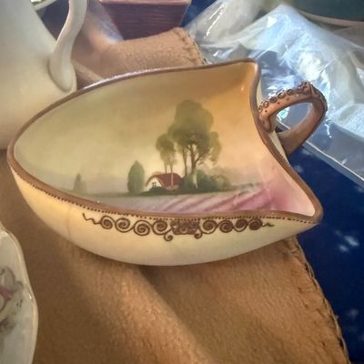 Sale Photo Thumbnail #6: Antique hand-painted porcelain leaf-shaped dish featuring a scenic landscape with a cottage, raised beaded scrollwork along the rim, and a small loop handle.