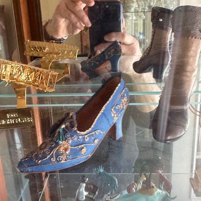 Sale Photo Thumbnail #124: Collection of miniature shoe figurines, including an ornate blue embroidered pump and Victorian-style lace-up boots, displayed inside a glass cabinet.