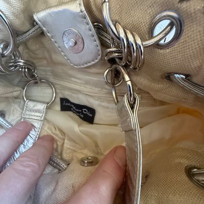 Sale Photo Thumbnail #184: Interior detail of a Lake Shore Drive brand metallic silver and cream canvas handbag, showing magnetic snap closure and ring hardware.