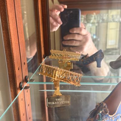 Sale Photo Thumbnail #125: Gold-tone miniature display model of a 1903 Wright Flyer mounted on a glass shelf inside a curio cabinet.