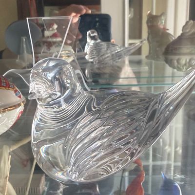 Sale Photo Thumbnail #128: Clear art glass bird figurine featuring detailed feather texturing, displayed on a glass cabinet shelf.