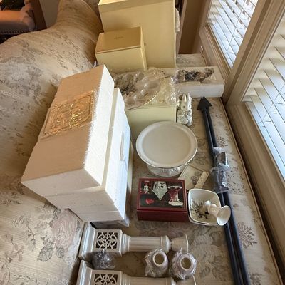 Sale Photo Thumbnail #43: Collection of home decor items and collectibles arranged on a floral upholstered sofa, including Lenox boxed pieces, ceramic candleholders, and a cake stand.