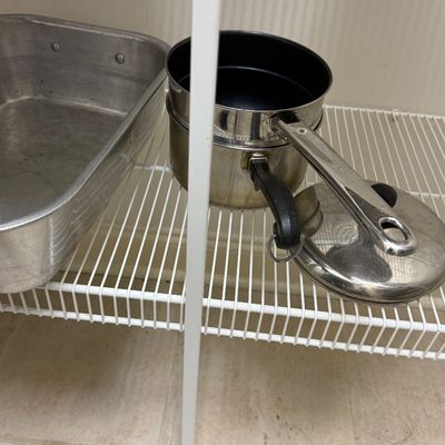 Sale Photo Thumbnail #85: Selection of metal cookware, including a stainless steel double boiler set with a lid and a large aluminum roasting pan, resting on wire shelving.