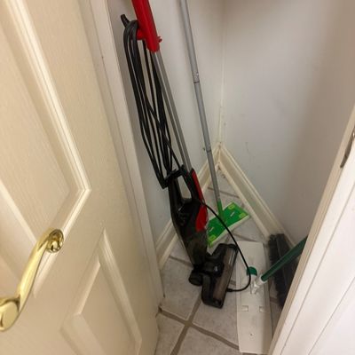 Sale Photo Thumbnail #100: Collection of cleaning supplies including a red and black stick vacuum cleaner, Swiffer mops, and a broom stored in a closet corner.