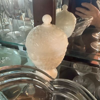 Sale Photo Thumbnail #106: Vintage white milk glass covered candy dish with a raised floral pattern and round finial lid, displayed inside a glass cabinet alongside other glassware.