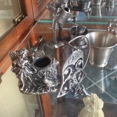 Sale Photo Thumbnail #139: Collection of vintage pewter figurines and small metal decor items displayed on glass cabinet shelves.