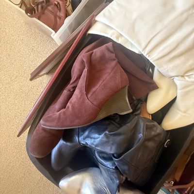 Sale Photo Thumbnail #190: Collection of women's boots and shoes in a storage tub, including maroon suede wedge boots, metallic silver mules, and black leather boots.