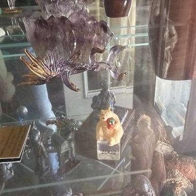 Sale Photo Thumbnail #133: Collection of glass and metal collectibles on display in a cabinet, including a large purple amethyst geode cluster, a iridescent glass dragons sculpture, and a 2002 polar bear figurine.
