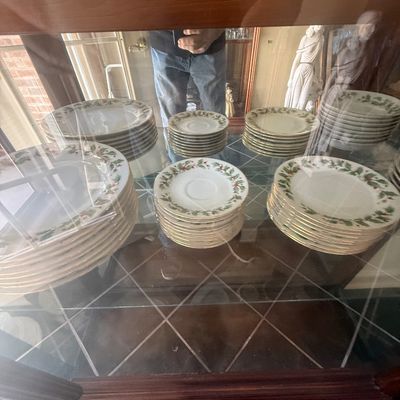Sale Photo Thumbnail #149: Large collection of porcelain holiday dinnerware featuring a holly pattern and gold rim accents, neatly stacked inside a glass cabinet shelf.