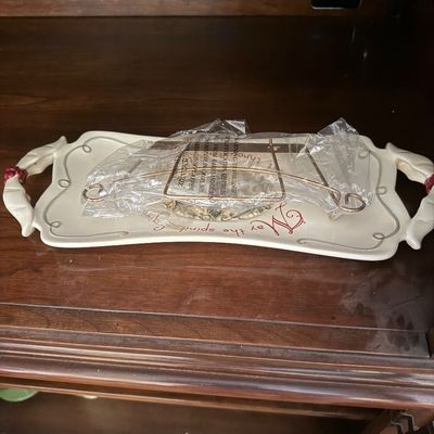 Sale Photo Thumbnail #39: Holiday ceramic serving tray with ribbon handles, featuring cursive red lettering and a metal display stand wrapped in plastic.