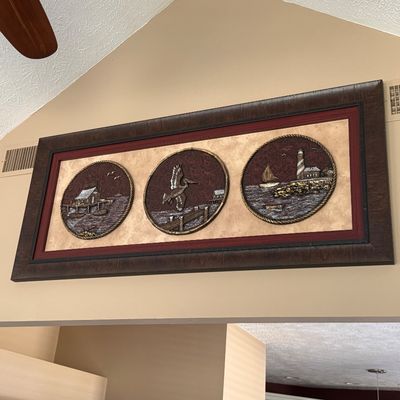 Sale Photo Thumbnail #78: Large framed nautical wall art piece featuring three circular 3D bas-relief panels depicting coastal scenes of a dock house, pelican, and lighthouse.