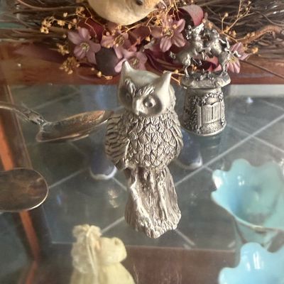 Sale Photo Thumbnail #140: Collection of decorative pewter miniatures including a detailed owl figurine and a thimble topped with rearing horses, displayed alongside a decorative bird wreath.