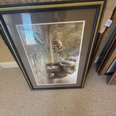 Sale Photo Thumbnail #176: Framed wildlife art print depicting African elephants in a savanna landscape, presented in a dark ornate frame with gold inner trim and a wide brown mat.