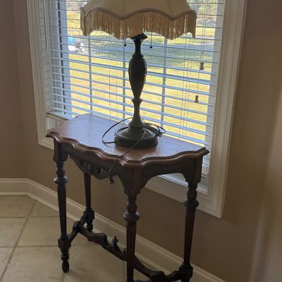 Sale Photo Thumbnail #60: Vintage dark wood console table with turned legs and carved apron details, paired with a table lamp featuring a fringe-trimmed fabric shade.