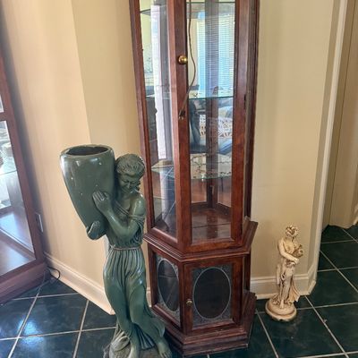 Sale Photo Thumbnail #30: Tall hexagonal mahogany display cabinet with glass shelving alongside classical-style maiden statues.