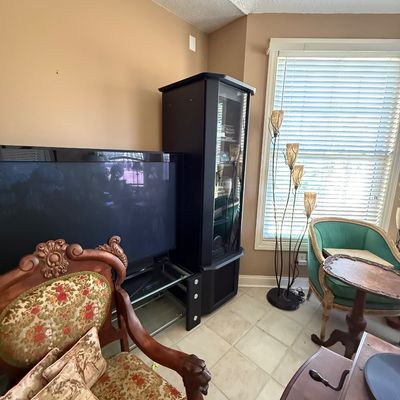 Sale Photo Thumbnail #71: Living room filled with eclectic furniture including a carved wood tapestry arm chair, black display cabinet, flat-screen TV, multi-light floor lamp, and a teal accent chair.