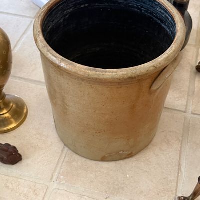 Sale Photo Thumbnail #76: Antique stoneware crock with a dark glazed interior and integrated side handles, showing minor wear and glaze loss near the base.