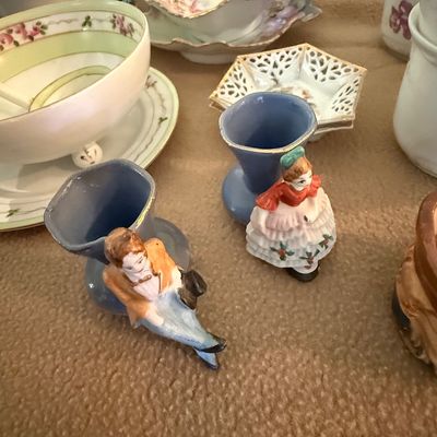 Sale Photo Thumbnail #44: Pair of vintage porcelain novelty match holders featuring seated Victorian-style figures next to blue vases, surrounded by various floral china tableware.