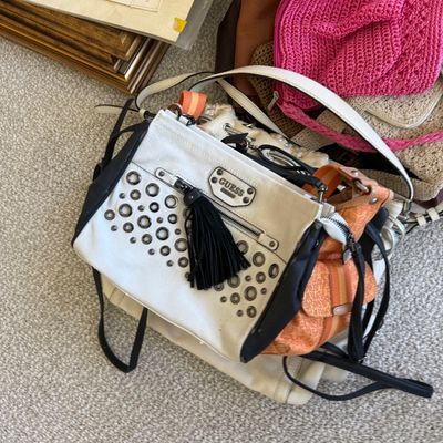 Sale Photo Thumbnail #180: Collection of women's handbags including a studded white Guess purse with black tassel detail, an orange printed crossbody, and a pink crochet bag.