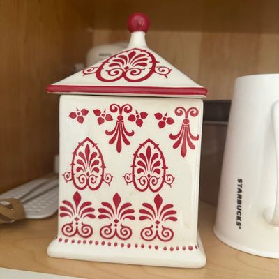 Sale Photo Thumbnail #12: Square white ceramic canister with a matching lid, decorated with red damask and scrollwork patterns, pictured inside a cabinet next to a Starbucks mug.