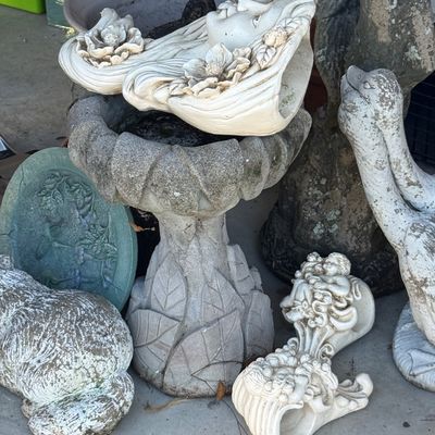 Sale Photo Thumbnail #17: Collection of concrete garden ornaments and planters, including a pediment birdbath, a maiden face planter, and animal statues with weathered outdoor patina.