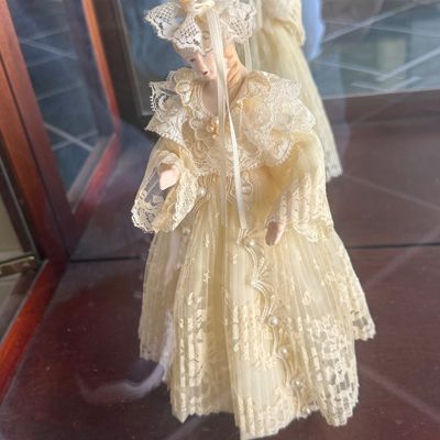 Sale Photo Thumbnail #121: Vintage porcelain musical doll or figurine wearing a detailed cream lace gown with pearl accents, displayed inside a glass cabinet.