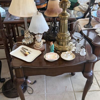 Sale Photo Thumbnail #62: Traditional Queen Anne style wooden end table with cabriole legs, displaying various vintage table lamps, small porcelain trinkets, vanity items, and glass perfume bottles.