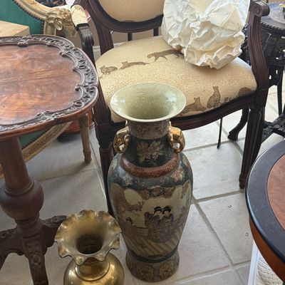 Sale Photo Thumbnail #72: Large Satsuma-style porcelain floor vase with geisha motifs, displayed alongside a brass urn-style vase and an armchair with big cat upholstery.